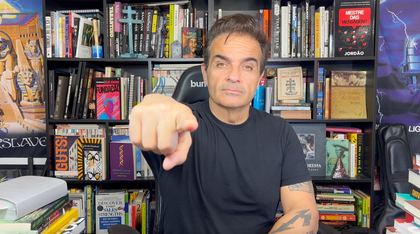 Jordão em frente à sua biblioteca, apontando para a câmera durante uma aula