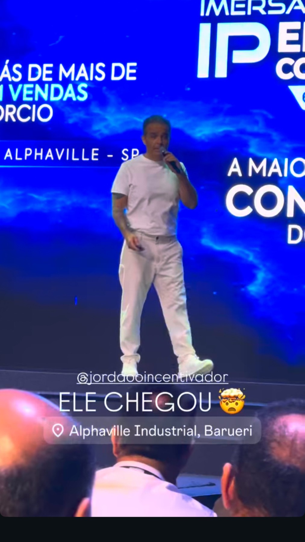 Jordão de microfone na mão durante uma palestra, diante de um telão azul